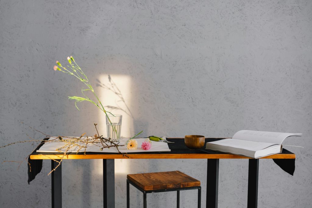 pexels-photo-6933429-6933429 A minimalist scene of a table with flowers, an open book, and wooden bowl, enhanced by natural lighting.